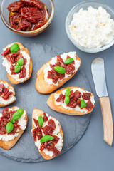 Bruschetta with sun dried tomato, feta and philadelphia cheese and basil on stone plate, vertical, top view, closeup
