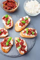 Bruschetta with sun dried tomato, feta and philadelphia cheese and basil on a stone plate, vertical, top view, closeup