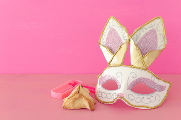 Purim celebration concept (jewish carnival holiday) with cute rabbit mask, noisemaker and hamantash cookies over wooden table