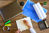 Female hand in a shirt writes in a leather notebook. Computer, cup of coffee, graphics, drawings, calculator on the table in the office. Business and Finance.