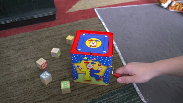 A woman's hand winding a jack-in-the-box toy until it pops up