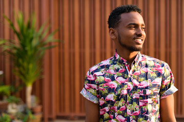 Face of happy young African tourist man thinking outdoors