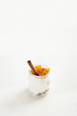 Jars of greek yogurt with granola, cinnamon and canned apricots on white background, vertical oriented