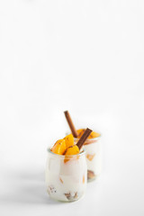 Jars of greek yogurt with granola, cinnamon and canned apricots on white background, vertical oriented. Heaithy food concept.
