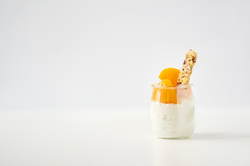 Jar of yogurt or curd with granola and canned apricots on white background
