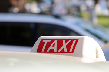 Taxi light sign or cab sign in white and red color with white text on the car roof at the street blurred background