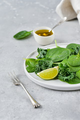 flat lay green salad of organic spinach and kale leaves with lemon juice and olive oil. diet menu concept, healthy food, save space, selective focus, light background