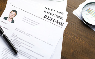 Resume (curriculum vitae, cv) and pen on a written wooden table.