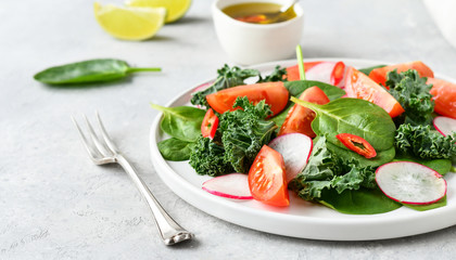 fresh salad of organic spinach, kale, red tomatoes and radish with olive oil and lime juice. healthy eating concept. diet, vegan cuisine. light background, selective focus