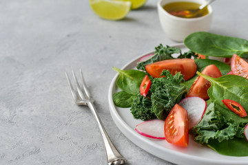 fresh salad of organic spinach, kale, red tomatoes and radish with olive oil and lime juice. healthy eating concept. diet, vegan cuisine. light background, selective focus