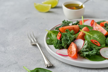 fresh salad of organic spinach, kale, red tomatoes and radish with olive oil and lime juice. healthy eating concept. diet, vegan cuisine. light background, selective focus
