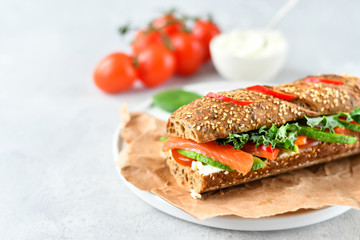 sandwich from a cereal baguette with avocado, salmon, cream cheese, tomatoes and lettuce leaves on a white plate.  light background, selective focus and copy space