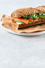 sandwich from a cereal baguette with avocado, salmon, cream cheese, tomatoes and lettuce leaves on a white plate.  light background, selective focus and copy space