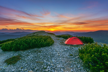 Spring on the mountainous valleys in the Ukrainian Carpathians overlooking the high snow-capped peaks covered with fogs against the backdrop of a tourist red tent