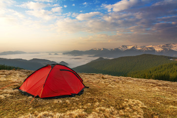 Spring on the mountainous valleys in the Ukrainian Carpathians overlooking the high snow-capped peaks covered with fogs against the backdrop of a tourist red tent