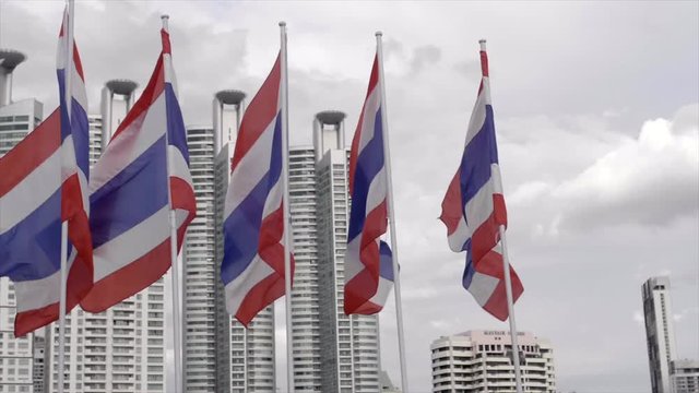The Kingdom of Thailand flags waving in the wind in front of high rise buildings
