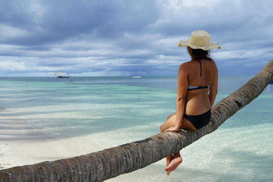 Asian woman sitting on a coconut tree branch, overlooking the ocean in Siquijor Island, Philippines