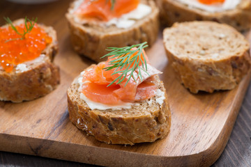 toasts with salted salmon and red caviar on wooden board, close-up