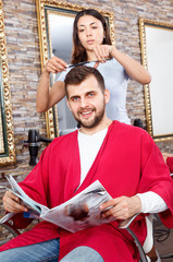 Cheerful woman professional hairdresser cut male's hair in hairdressing salon