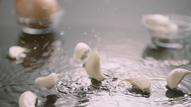 Garlic cloves splashing into water on a clean surface.