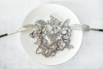 Obraz na płótnie Canvas Many sparkling jewelery on a white plate with a knife and fork. The concept of luxury life, wealth, glamor, fashion and weddings