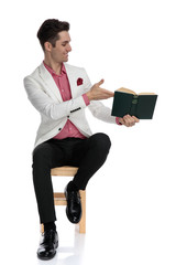 smiling young man recommending a book to  side while sitting