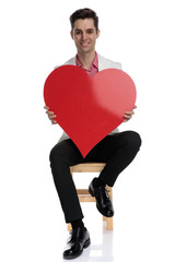 smiling young smart casual man sitting and holding a  heart
