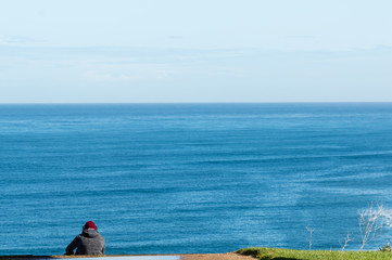 Young man listening music is sitting on cliff's edge of the sea. With a blue sky background in a spring day.
