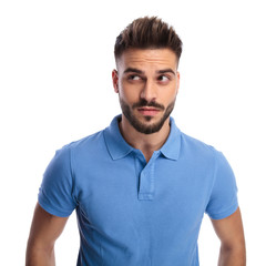 Obraz premium Thoughtful young man wearing a light blue polo looking upwards at a side