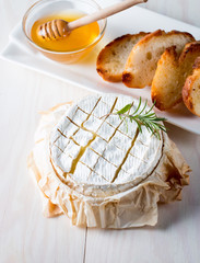 Baked camembert cheese. Fresh Brie cheese and a slice on a wooden board with nuts, honey, rosemary,...