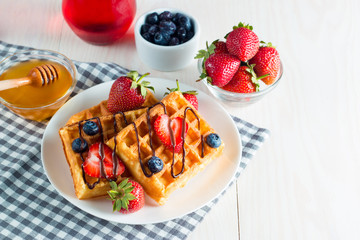 Photo of fresh homemade food made of berry Belgian waffles with honey, chocolate, strawberry, blueberry, maple syrup and cream. Healthy dessert breakfast concept with juice. 
