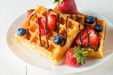 Photo of fresh homemade food made of berry Belgian waffles with honey, chocolate, strawberry, blueberry, maple syrup and cream. Healthy dessert breakfast concept with juice. 