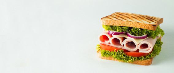 Close-up photo of a club sandwich. Sandwich with meat, prosciutto, salami, salad, vegetables, lettuce, tomato, onion and mustard on a fresh sliced rye bread on wooden background. Olives background.
