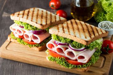 Close-up photo of a club sandwich. Sandwich with meat, prosciutto, salami, salad, vegetables, lettuce, tomato, onion and mustard on a fresh sliced rye bread on wooden background. Olives background.