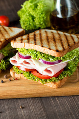 Close-up photo of a club sandwich. Sandwich with meat, prosciutto, salami, salad, vegetables, lettuce, tomato, onion and mustard on a fresh sliced rye bread on wooden background. Olives background.