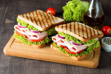 Close-up photo of a club sandwich. Sandwich with meat, prosciutto, salami, salad, vegetables, lettuce, tomato, onion and mustard on a fresh sliced rye bread on wooden background. Olives background.