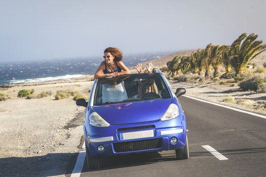 Summer vacation and travel concept image of two young woman in a convertible car. Curly brunette out of open roof. Friends having fun in a cabriolet topless. Female enjoying freedom vacation