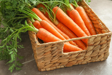 Wicker basket with ripe carrots on grey table, closeup