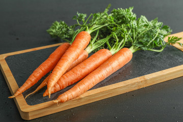 Cutting board with ripe carrots on black table, space for text