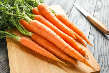 Cutting board with ripe carrots and knife on wooden table