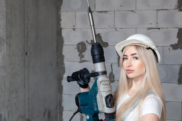 Closeup blonde girl foreman in white construction helmet holding professional perforator, drill in...