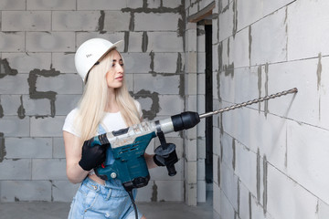 Closeup blonde girl foreman in white construction helmet holding professional perforator, drill in...