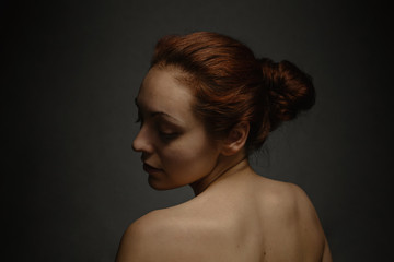Tan woman with ginger hair close her eyes and posing on a camera. The view from the back. Dark background