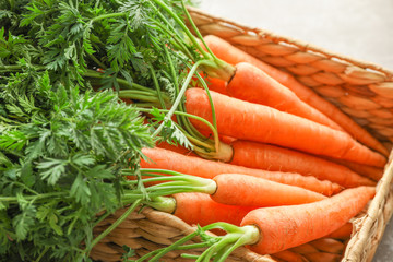 Wicker basket with ripe carrots on grey table, closeup