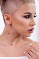 Closeup sexy blonde model with bright make-up, bare shoulders and short hair with shaved temples in modern round silver jewelry earrings and necklace. Сoncept shooting for bijouterie store