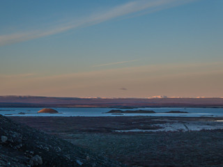Sunrise over lava fields. Soft colors of the sky. High mountains in the back covered with snow. Lake in the middle, shines bright. Volcanic landscape, alienation and solitude. Harsh conditions.
