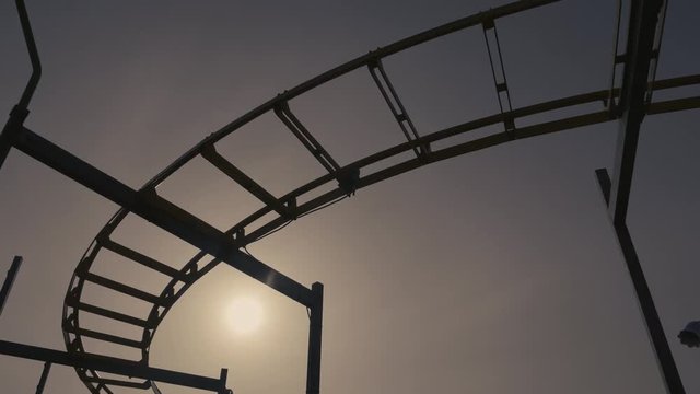 Silhouette of a rickety old roller coaster nearing sunset, camera pans