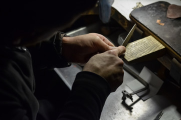 The master jeweler holds the working tool in his hands and makes jewelery at his workplace in the jewelry workshop.