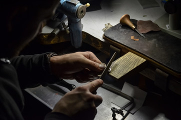 The master jeweler holds the working tool in his hands and makes jewelery at his workplace in the...