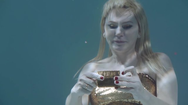 Close-up shot of a blonde girl opening a small chestbox underwater, aqua story.